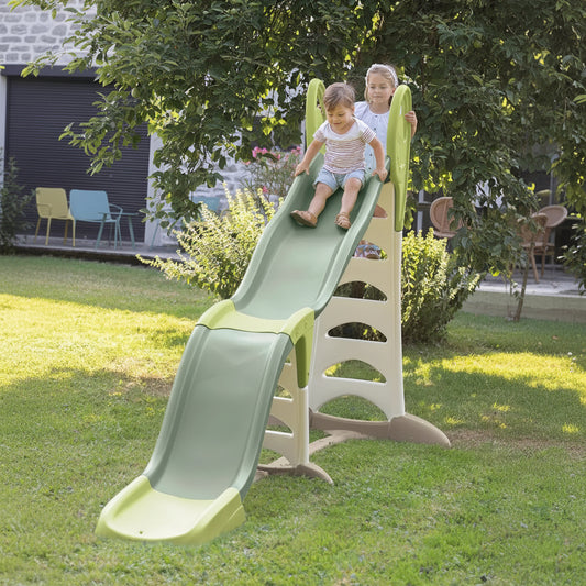Two children playing on a green slide in a garden setting.
