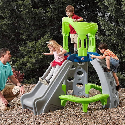 kids outdoor playhouse Qatar -Children playing on a green and gray playground structure with a man observing.