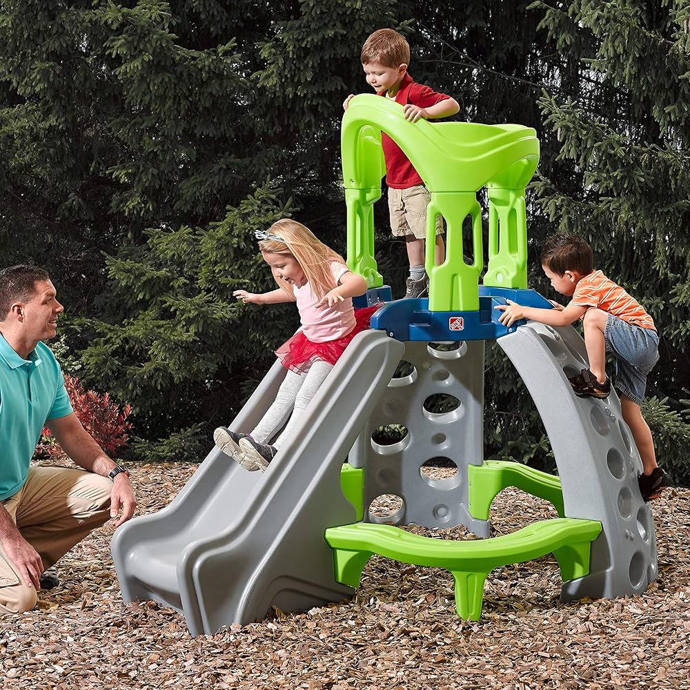 kids outdoor playhouse Qatar -Children playing on a green and gray playground structure with a man observing.