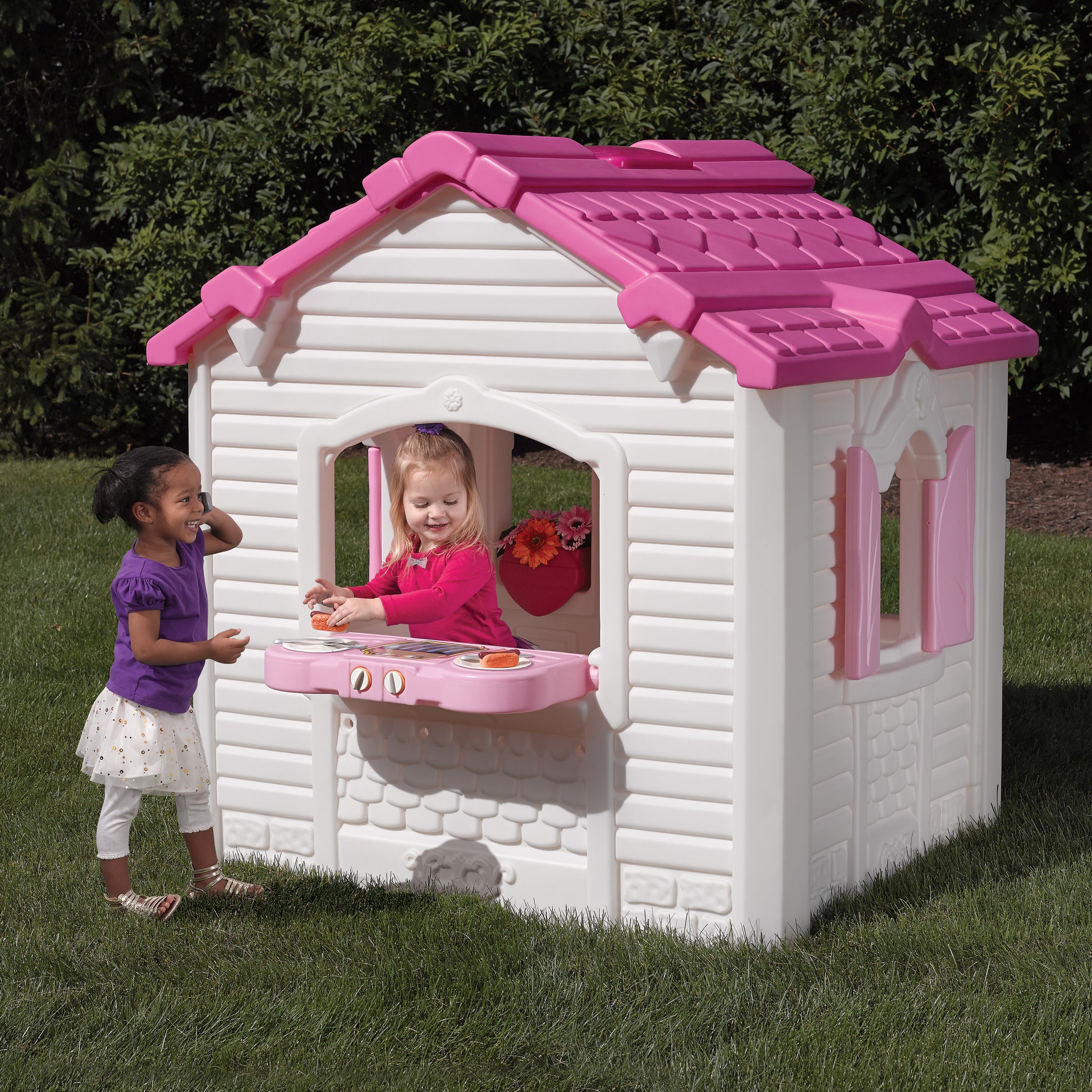 kids outdoor playhouse Qatar -Children playing inside a pink and white playhouse on grass with trees in the background